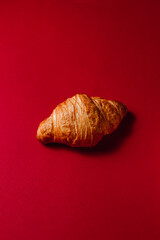 A golden fresh and soft croissant on a red background with room for text. Creative design of crispy pastries for bakery and coffee shop. Delicious desserts for breakfast and for the holiday