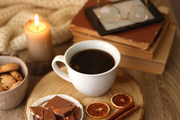 Bowl of cookies, cup of tea or coffee, chocolate, spices, knitted blanket, books, glasses and candle on the table. Cozy hygge atmosphere at home. Selective focus.