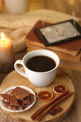 Bowl of cookies, cup of tea or coffee, chocolate, spices, knitted blanket, books, glasses and candle on the table. Cozy hygge atmosphere at home. Selective focus.