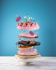 Flying cake layers with berries,chocolate,macarons,pink cream,festive burning candles on blue...