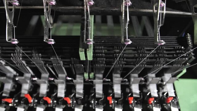 Close up of textile machine in slow motion. Fibre thread lines on the weaving loom machine. A loom machine for clothing or woven clothes. Weaving machine for garment industry.