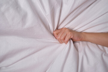 A woman clutches a white sheet blanket with her hand. Love, orgasm of a woman in the bedroom
