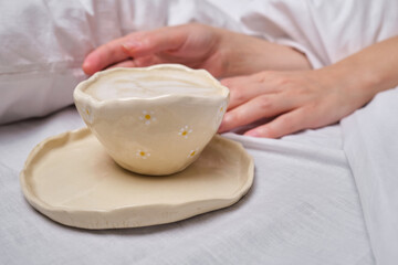 A woman is holding a cup of coffee while sitting on the bed. A cup of aromatic coffee on a bed with white linens. Morning coffee concept