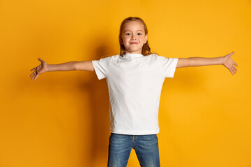 Portrait of little beautiful girl, child in white T-shirt posing isolated over yellow studio...