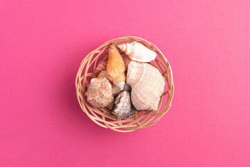 Top view of wicker basket with sea shells isolated on bright pink background.