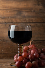 Glass of red wine with red grapes nearby, dark rustic background