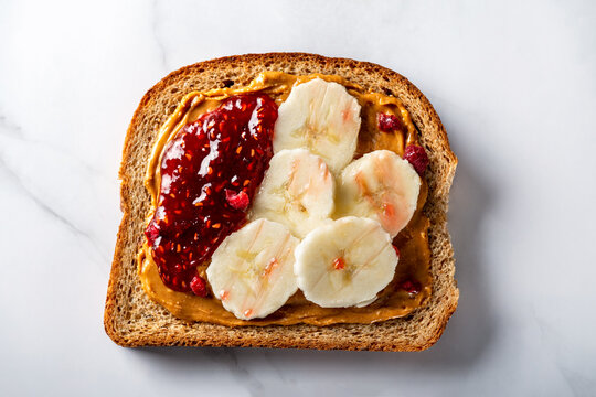 Open Sandwich From Slice Of Wholegrain Bread With Peanut Nut Butter, Bananas And Raspberry Jam