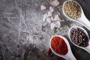 White spoons with spices on slate stone and copy space