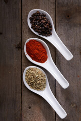 Three white spoons with spices on rustic wood