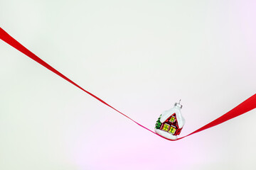 Minimalistic Christmas card. Christmas tree toy winter house on a red ribbon. Happy New Year 2023. Merry Christmas greetings.