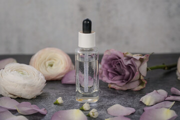 Obraz na płótnie Canvas Natural homemade face serum in transparent glass dropper bottle on grey marble background with dusty pink roses. 