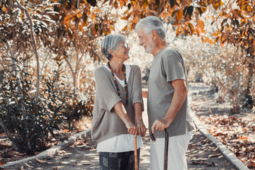 Beautiful white-haired senior couple walking in the woods with help of a walking cane. Smiling...