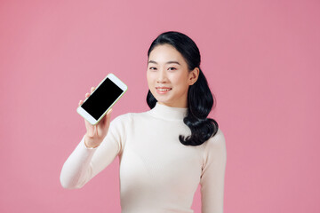 Beautiful Asian woman holding blank screen smartphone on pink background