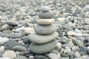 Fototapeta na wymiar Stone Cairn on Grey Pebble Sea Background. Rock Zen Sculpture