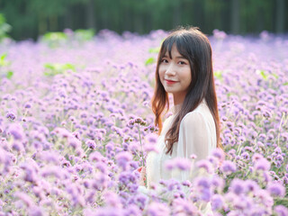 Beautiful woman in white dress standing among purple Verbena Bonariensis flower field, charming Chinese girl with black long hair enjoy her leisure time outdoor, backlit effect.