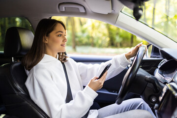 Beautiful young businesswoman sending a text while driving to work