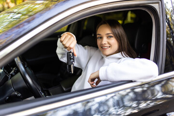 Young woman new car owner smiling and showing keys in driver seat