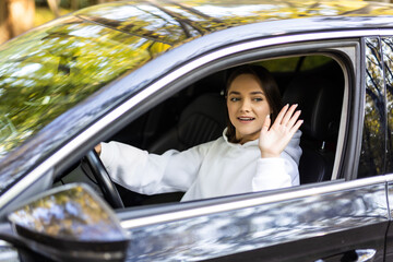 Young woman greeting with hand from car. Cheerful caucasian girl welcome somebody sitting in car