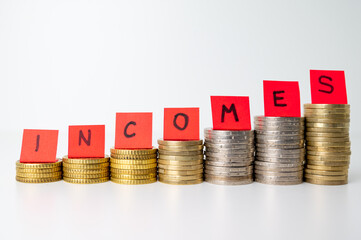 Stacks of coins, and above them red tickets that make up the word "incomes". Increase in revenues, earnings, and economic consequences. Increase in income and speculation
