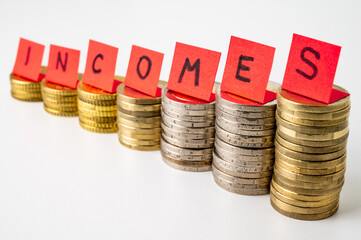 Stacks of coins, and above them red tickets that make up the word "incomes". Increase in revenues, earnings, and economic consequences. Increase in income and speculation
