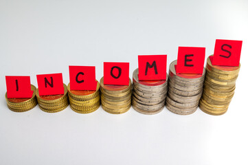 Stacks of coins, and above them red tickets that make up the word "incomes". Increase in revenues, earnings, and economic consequences. Increase in income and speculation
