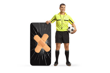 Full length portrait of a football referee standing next to a smartphone with broken screen fixed...