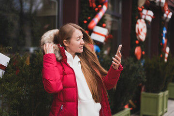 beautiful woman in winter clothes walks down the street decorated with New Year's decor and communicates by phone