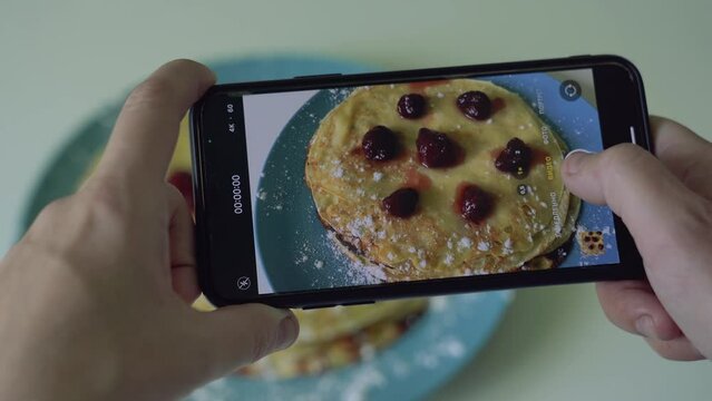Woman makes photo of cooked pancakes with raspberries and sugar powder served on blue plate.