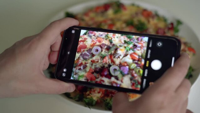 Woman takes picture of cooked pizza on plate at table. Extreme closeup