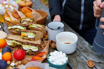 picnic in the autumn season, food on a wooden table, hot tea, pastries and sandwiches