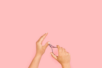 Manos de mujer arreglandose las uñas sobre un fondo rosa pastel. Vista superior y de cerca. Copy space