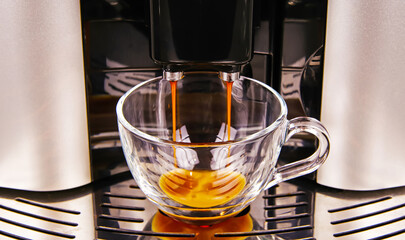 Closeup of modern fully automatic coffee maker machine outlet, one isolated transparent glass cup...