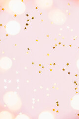 Christmas festive background. Gold party decorations, confetti stars, christmas lights on pastel pink background. Christmas, winter holiday, new year concept. Flat lay, top view, copy space.
