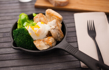 pieces of fried chicken breast with boiled broccoli and poached egg in cast iron portioned skillet