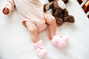 Newborn baby girl in knitted shoes with a bow on a white blanket. Childhood concept.