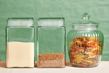 Colored penne, semolina and buckwheat in transparent jars on the kitchen table