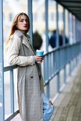 Young stylish woman drinking coffee in a city street. Hipster European girl with latte paper glass in street. Gorgeous young woman with cup of coffee in city street. Coffee break. Coffee to go.
