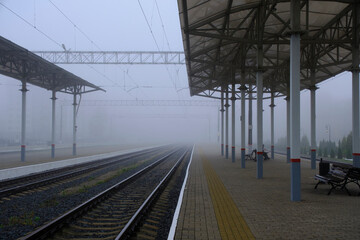 Empty platform at station and rails going into fog.