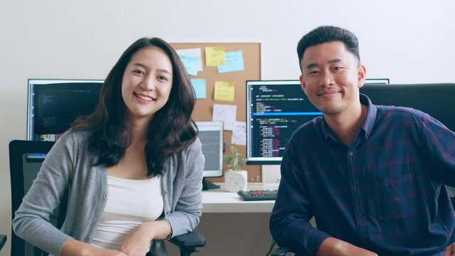 Portrait young Asian woman developer programmer, software engineer, IT support, with colleague look at camera and smile enjoy working at office together.