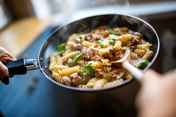 woman hand cooking tasty chicken fillet with mushroom in a creamy sauce with fusilli pasta in pan on kitchen