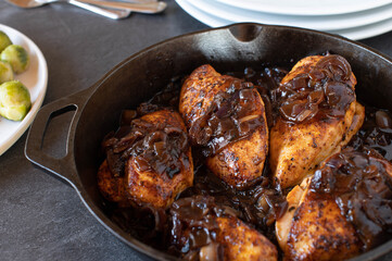Baked chicken breast with red onion sauce in a cast iron pan on kitchen table