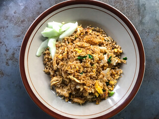 Top view of traditional nasi goreng (Indonesian Fried Rice), served with cucumber pickles on a round plate.