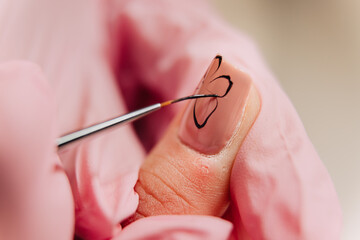 Manicure process. A master manicurist makes a drawing on artificial nails using black varnish and a thin brush.