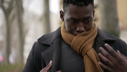 Black man putting scarf outdoors in winter season. African guy adjusting scaf in the cold wearing coat
