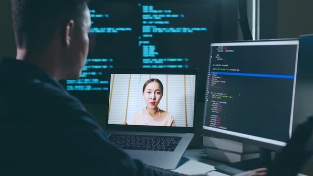 Asian man developer programmer, software engineer, IT technical support center talking with team via video call. Working on computer overtime to check coding in bugging system