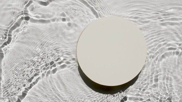 Empty white circle podium on transparent clear water texture with waves in sunlight. Background for product presentation. Flat lay cosmetic mockup, copy space. High quality 4k footage