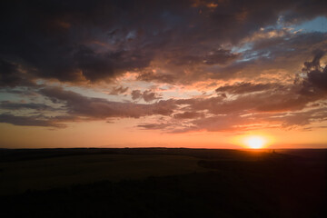 Bright colorful sunset sky with setting sun and vibrant clouds over dark landscape