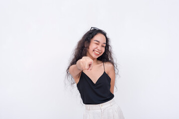 A confident and carefree young asian woman points to the camera while winking. Isolated on a white background.