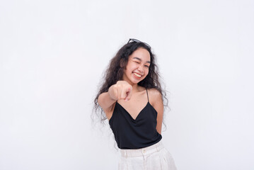 A confident and carefree young asian woman points to the camera while winking. Isolated on a white...