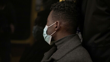 Black man commuter inside subway metro looking out window wearing covid-19 face mask